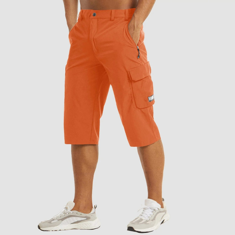 Laden Sie das Bild in Galerie -Viewer, Mann trägt orange Cargo-Shorts und weiße Sneaker, seitliche Taschen, sportlicher Look, ideal für Sommermode und Outdoor-Aktivitäten.
