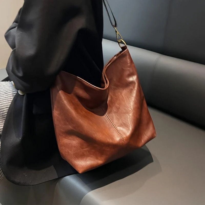 Laden Sie das Bild in Galerie -Viewer, Braune Ledertasche auf grauem Sofa, modernes Design, Damenmode-Accessoire, eleganter Look, hochwertige Handtasche, stilvoll und zeitlos.
