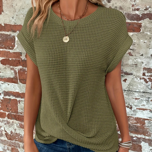 Grünes, strukturiertes Damen-T-Shirt mit kurzen Ärmeln vor einer Backsteinwand. Modisches Freizeitoutfit, ideal für Sommer und Frühling.