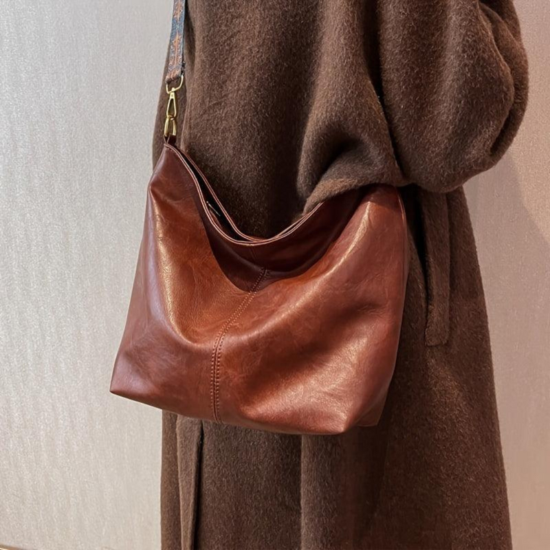 Laden Sie das Bild in Galerie -Viewer, Braune Ledertasche über der Schulter einer Person in braunem Mantel, elegantes Design, hochwertige Handtasche, modisches Accessoire für Damen.
