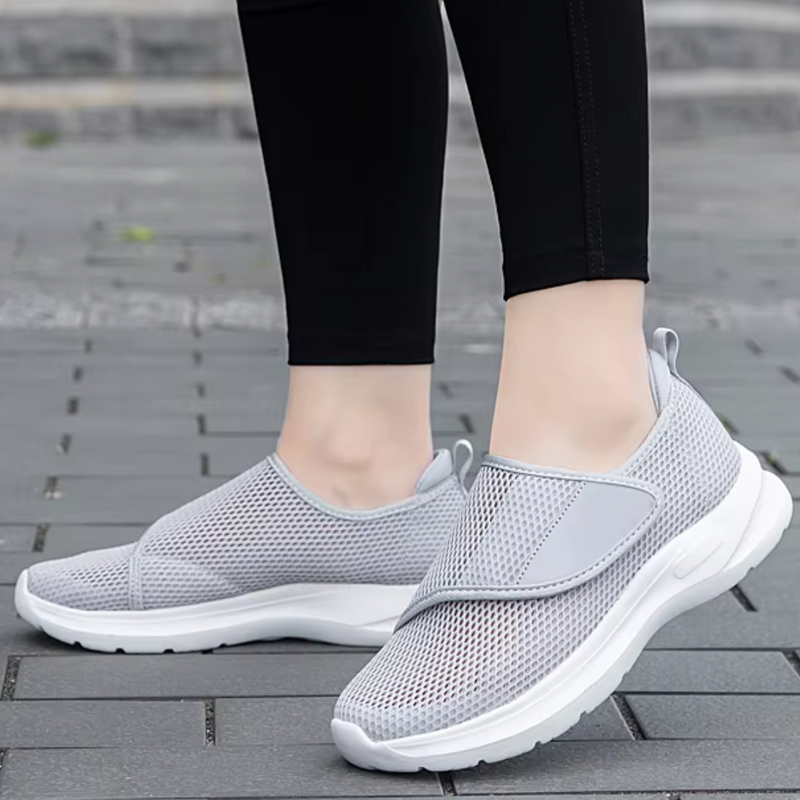 Laden Sie das Bild in Galerie -Viewer, Graue Damen-Sneaker mit Mesh-Oberfläche, getragen auf Gehweg. Bequeme, atmungsaktive Sportschuhe für Freizeit und Sport.
