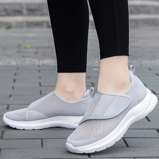 Graue Damen-Sneaker mit Mesh-Oberfläche, getragen auf Gehweg. Bequeme, atmungsaktive Sportschuhe für Freizeit und Sport.