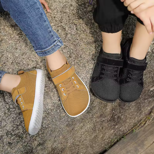 Zwei Paar Kinderschuhe auf Felsen: gelbe Sneaker mit Klettverschluss und schwarze Turnschuhe. Bequeme, modische Kinderschuhe für Outdoor-Aktivitäten.