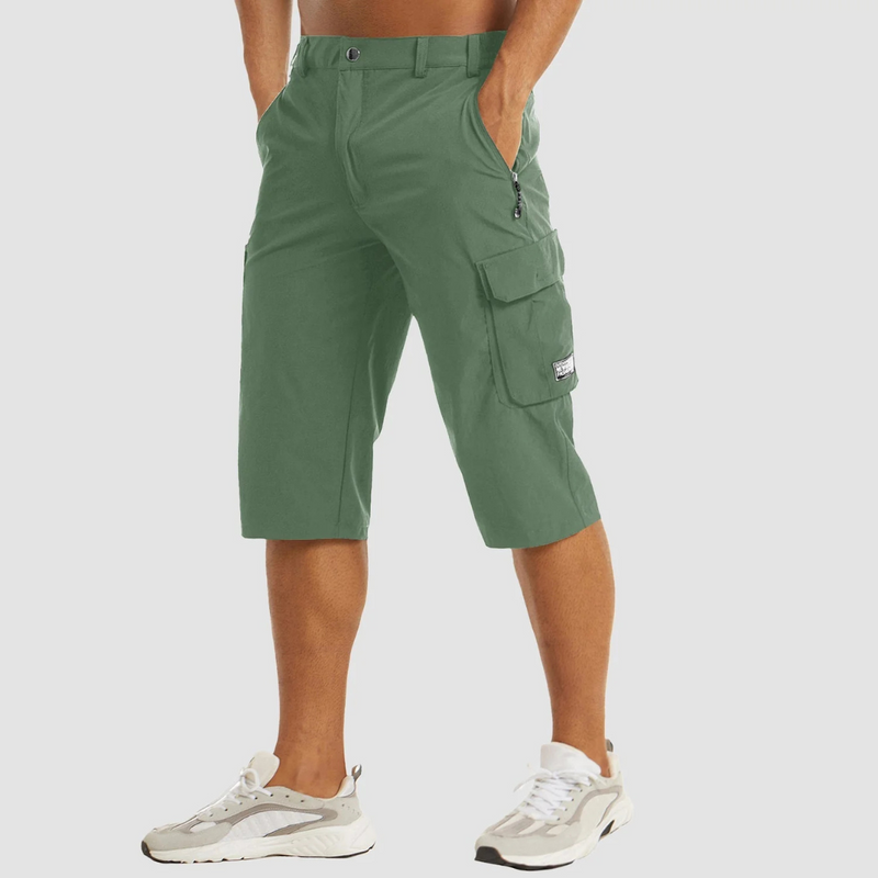 Laden Sie das Bild in Galerie -Viewer, Grüne Cargo-Shorts für Herren, knielang, mit Seitentaschen und Reißverschluss, kombiniert mit weißen Sneakers. Ideal für Freizeit und Outdoor.
