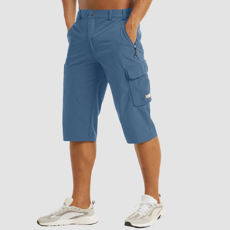 Laden Sie das Bild in Galerie -Viewer, Mann trägt blaue Cargo-Bermudashorts mit Taschen, kombiniert mit weißen Sneakers. Sommermode, lässiger Stil, Herrenbekleidung.

