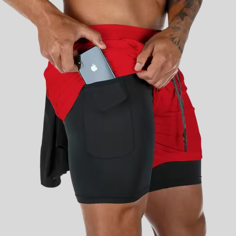 Laden Sie das Bild in Galerie -Viewer, Mann in roten und schwarzen Sportshorts mit Handytasche, steckt Smartphone ein. Fitnessmode, praktische Sportbekleidung, Herren-Shorts mit Tasche.
