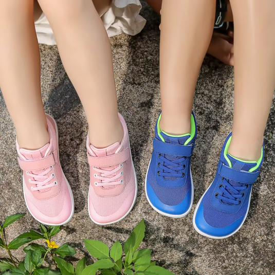 Zwei Paar Kinderschuhe auf Stein: rosa und blaue Sneaker mit Klettverschluss. Bequeme, modische Schuhe für Kinder, ideal für Freizeit und Spiel.
