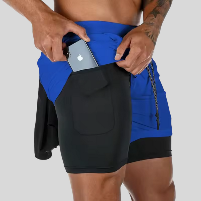 Laden Sie das Bild in Galerie -Viewer, Mann in blauen und schwarzen Sportshorts mit Smartphone in der Tasche, Fitnessbekleidung, praktisches Design, ideal für Sport und Freizeit.
