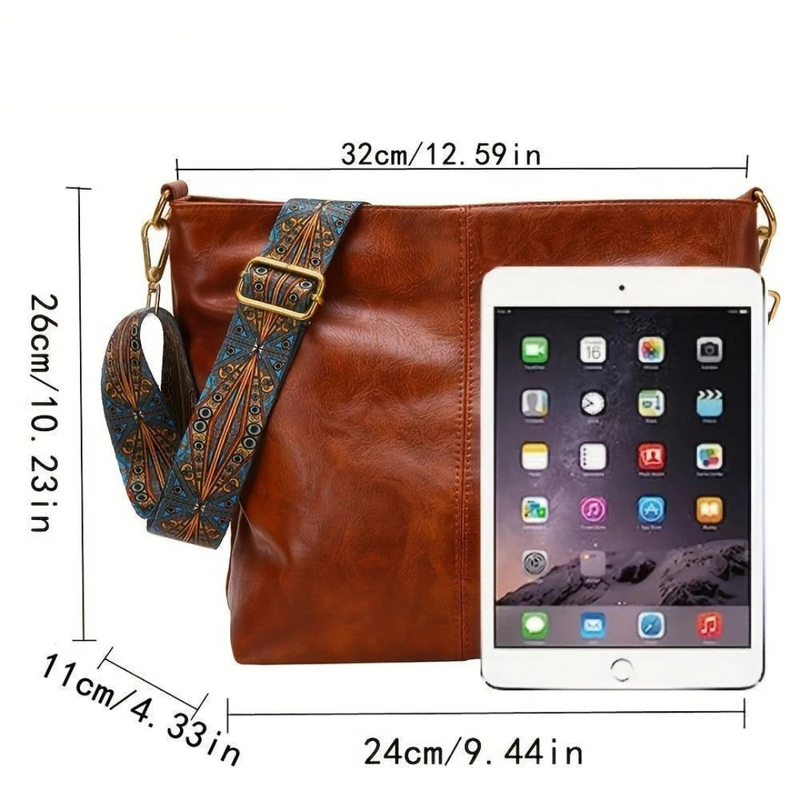 Laden Sie das Bild in Galerie -Viewer, Braune Ledertasche mit verstellbarem, gemustertem Schultergurt, neben einem Tablet. Maße: 32x26x11 cm. Modische Umhängetasche für Damen.
