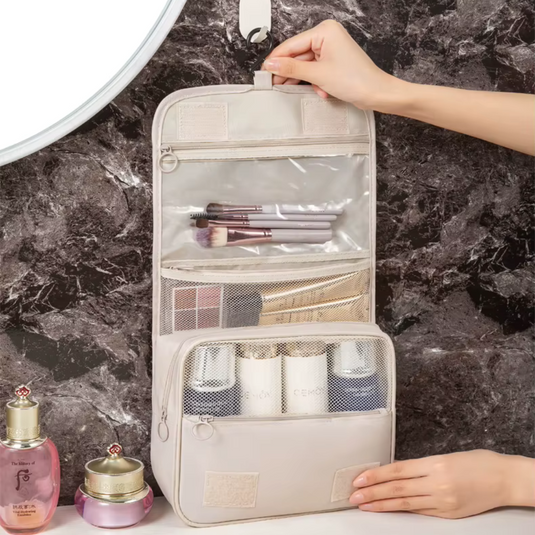 Hängender Kulturbeutel mit transparenten Fächern, gefüllt mit Kosmetikartikeln und Make-up-Pinseln, auf Marmorhintergrund. Ideal für Reisen und Badezimmer.