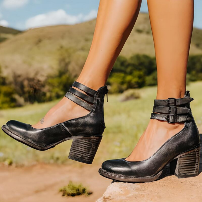 Schwarze Lederstiefeletten mit Blockabsatz und Schnallen, getragen von einer Person in einer natürlichen Landschaft. Modische Damenstiefel im Freien.