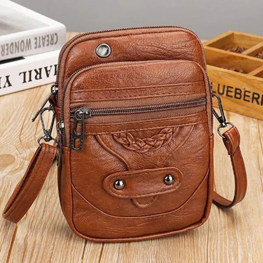 Braune Leder-Umhängetasche mit Reißverschluss und Knopfdetails auf Holztisch, ideal für Herrenmode, Accessoires, Vintage-Stil.