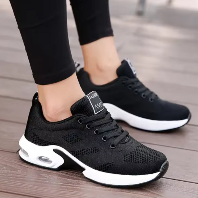 Schwarze Damen-Sneaker mit weißer Sohle, atmungsaktives Mesh-Design, ideal für Sport und Freizeit, modische Turnschuhe auf Holzfußboden.