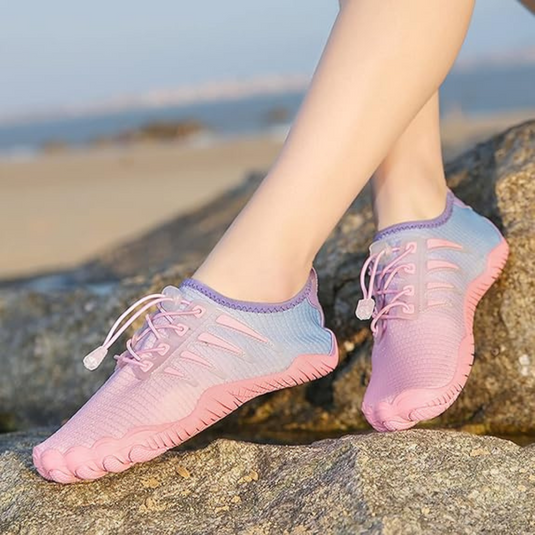 Füße in rosa-blauen Barfußschuhen auf Felsen am Strand. Leichte, atmungsaktive Sportschuhe für Outdoor-Aktivitäten und Fitness.