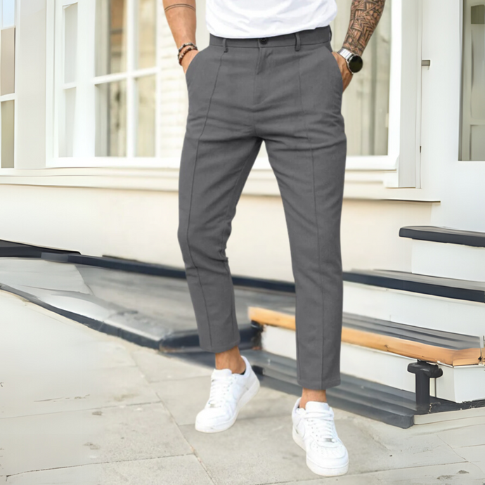 Mann in grauer Anzughose und weißen Sneakers steht vor modernem Gebäude. Stilvolle Herrenmode, urbane Eleganz, trendige Freizeitkleidung.
