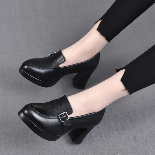 Schwarze Damenpumps mit Blockabsatz und Schnalle, getragen zu schwarzer Hose. Elegante, modische Schuhe für Büro oder Abendveranstaltungen.