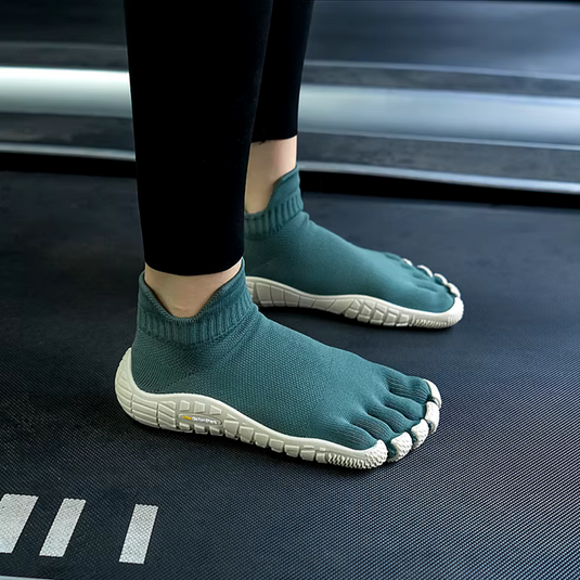 Person auf Laufband trägt grüne Zehenschuhe mit weißer Sohle, ideal für Barfußlauf und Fitness. Innovatives Design für natürliche Fußbewegung.