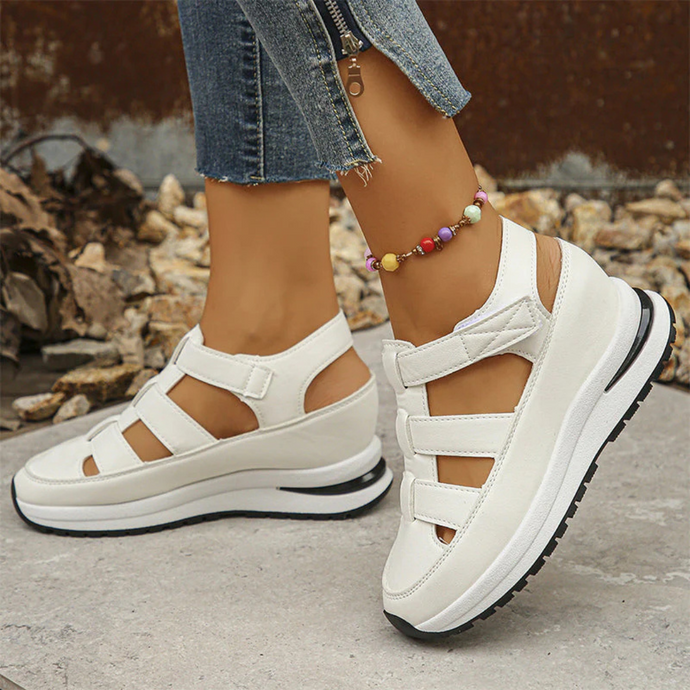 Weiße Plateau-Sandalen mit Klettverschluss an Frauenfüßen, kombiniert mit Jeans und buntem Fußkettchen. Ideal für Sommermode und Freizeitoutfits.
