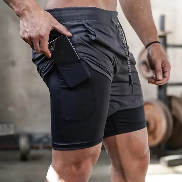 Mann in Sportshorts mit Smartphone-Tasche im Fitnessstudio. Funktionale Trainingsbekleidung, ideal für Workout und Laufen.