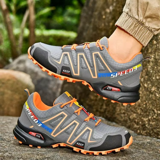 Graue Laufschuhe mit orangefarbenen Akzenten, robustem Profil und atmungsaktivem Mesh-Design, ideal für Outdoor-Aktivitäten und Trailrunning.
