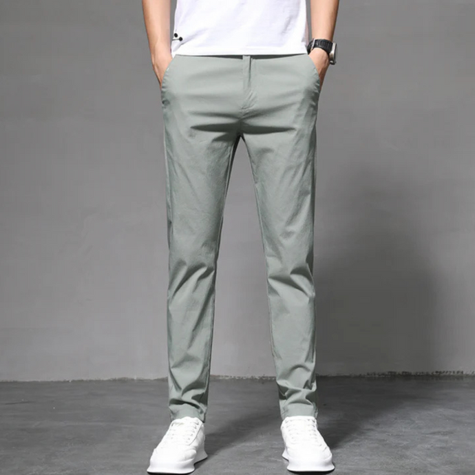 Mann trägt graue Chinohose und weiße Sneaker vor grauem Hintergrund. Modische Herrenbekleidung, lässiger Stil, moderne Herrenhose.