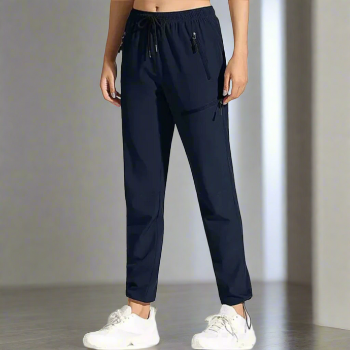 Damen Jogginghose in Dunkelblau, elastischer Bund, seitliche Taschen, sportlich-lässiger Stil, ideal für Fitness und Freizeit, kombiniert mit weißen Sneakers.