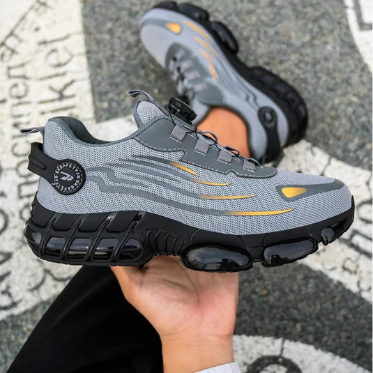 Grauer Sneaker mit schwarzer Sohle und gelben Akzenten, gehalten in einer Hand. Modernes Design, ideal für Sport und Freizeit.