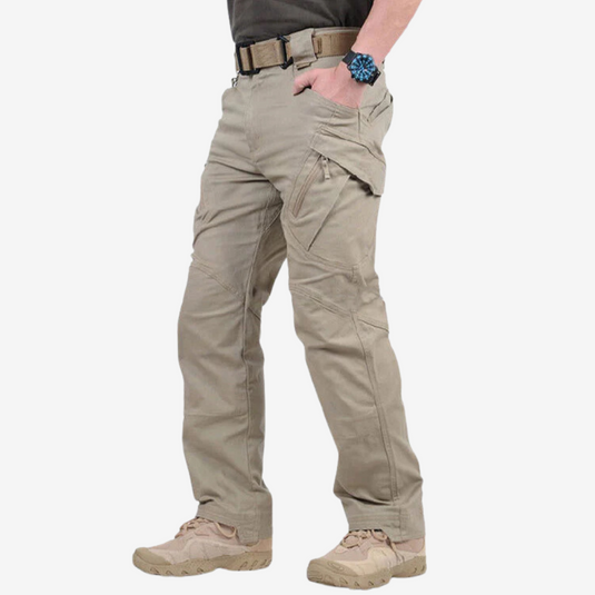 Mann trägt beige taktische Hose mit Taschen, Gürtel und Uhr. Outdoor-Bekleidung, strapazierfähige Cargohose, ideal für Abenteuer und Wandern.