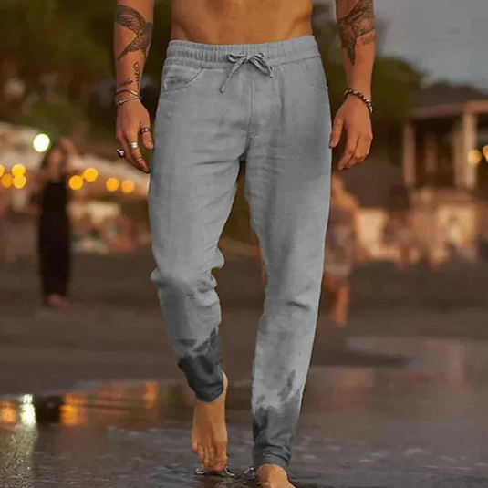 Mann in grauer Jogginghose spaziert barfuß am Strand bei Sonnenuntergang. Freizeitmode, Strandspaziergang, Herrenbekleidung.