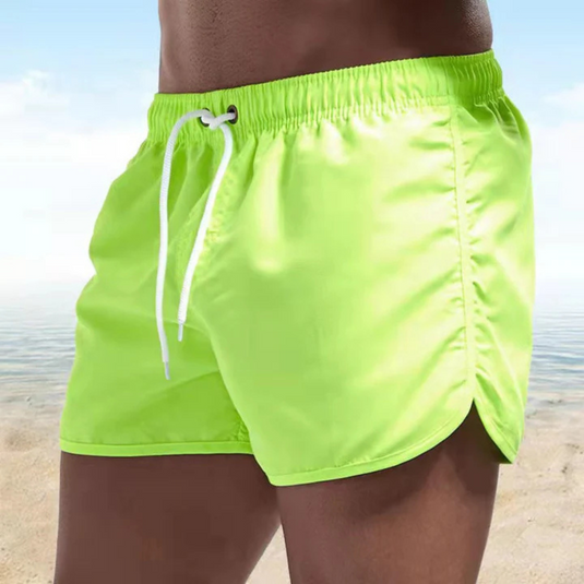 Neon-grüne Badeshorts am Strand, Herrenmode, Sommerbekleidung, leuchtende Farbe, elastischer Bund, Kordelzug, ideal für Strandurlaub.