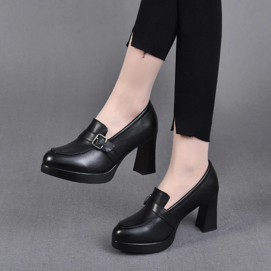 Schwarze Damenpumps mit Blockabsatz und Schnalle, getragen zu schwarzer Hose. Elegante, modische Schuhe für Büro oder Abendveranstaltungen.