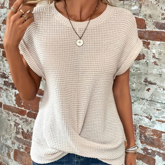 Damen T-Shirt aus grobem Strick in Beige, lässiger Stil, kombiniert mit Jeans, vor einer Backsteinwand. Perfekt für Freizeitmode und Sommeroutfits.