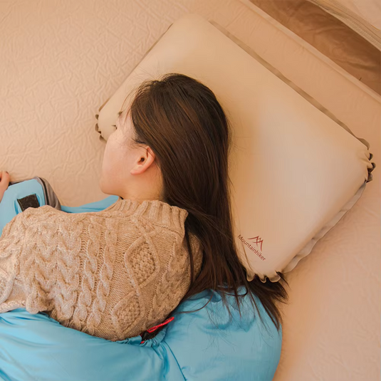 Frau schläft auf aufblasbarem Kissen im Schlafsack, Camping, Outdoor, bequem, tragbar, beige Kissen, blaue Decke, Entspannung, Erholung.
