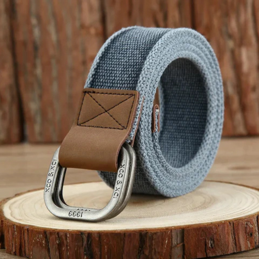 Grauer Stoffgürtel mit braunem Lederdetail und Metallschnalle, auf Holzscheibe präsentiert. Moderner Herrenmode-Accessoire, robust und stilvoll.