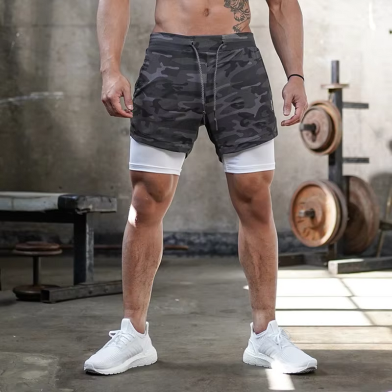 Laden Sie das Bild in Galerie -Viewer, Mann in Camouflage-Shorts und weißen Sneakers im Fitnessstudio, Hanteln im Hintergrund. Sportbekleidung, Fitnessmode, Workout-Outfit.
