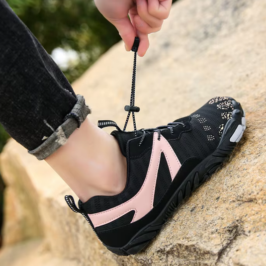 Person bindet schwarze Wanderschuhe mit rosa Akzenten auf einem Felsen. Outdoor-Schuhe, Trekking, robuste Sohle, Schnürsenkel, Natur.