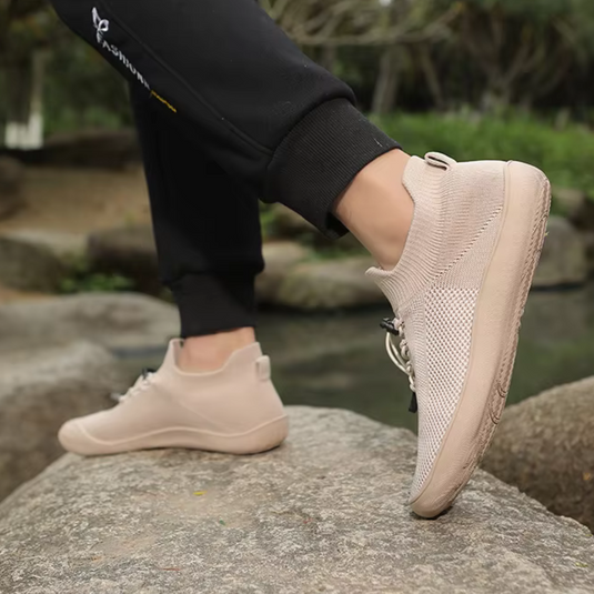 Beige Sneaker auf Felsen, getragen von Person in schwarzer Hose. Outdoor-Szene, modischer Freizeitschuh, ideal für Wanderungen und Spaziergänge.
