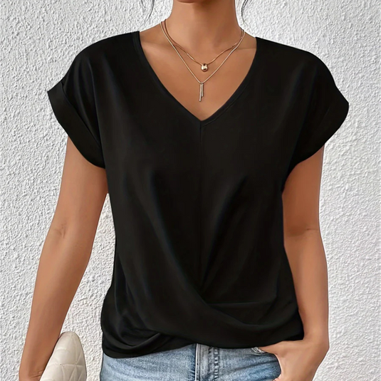 Frau in schwarzem V-Ausschnitt-T-Shirt, trägt zwei Halsketten, hält eine weiße Tasche, vor weißer Wand. Modetrend, lässiger Stil, Damenmode.