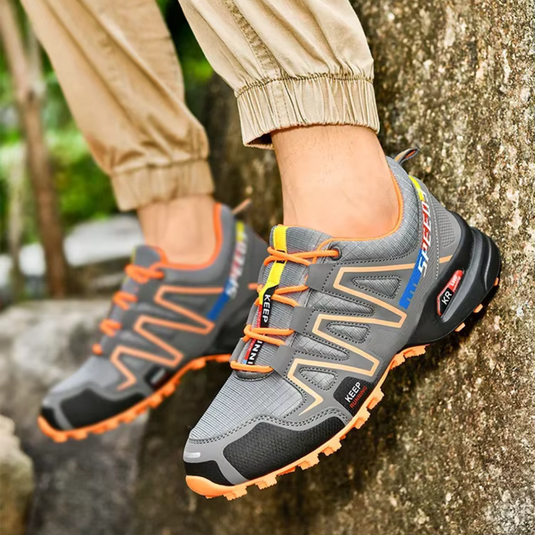 Graue Outdoor-Sneaker mit orangefarbenen Akzenten, robustem Profil und atmungsaktivem Mesh, ideal für Wandern und Trekking.