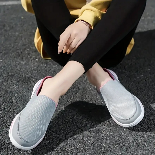 Frau in gelber Jacke und schwarzen Leggings trägt graue Slip-On-Sneaker auf Asphalt. Bequeme Freizeitschuhe, modisch, lässig.