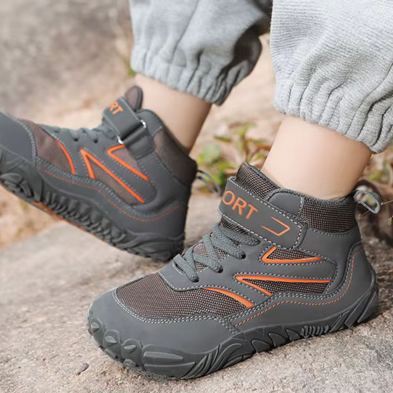 Laden Sie das Bild in Galerie -Viewer, Graue Kinderschuhe mit orangefarbenen Akzenten, robustes Design, Klettverschluss, ideal für Outdoor-Aktivitäten, auf Steinuntergrund.
