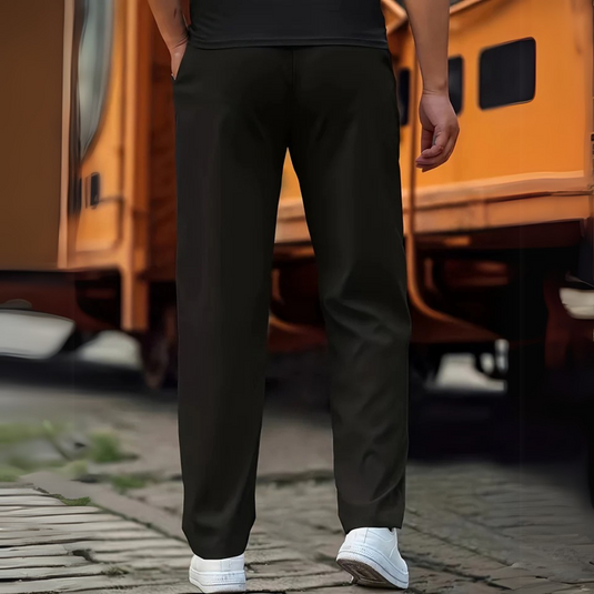 Hinteransicht einer Person in schwarzer Hose und weißen Sneakers vor einem orangefarbenen Zug. Urbaner Stil, Freizeitkleidung, Bahnhofsatmosphäre.