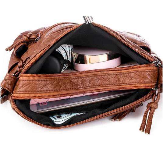 Offene braune Lederhandtasche mit Reißverschluss, gefüllt mit Smartphone, Kosmetik und Notizbuch. Damenmode, Accessoires, praktische Handtasche.