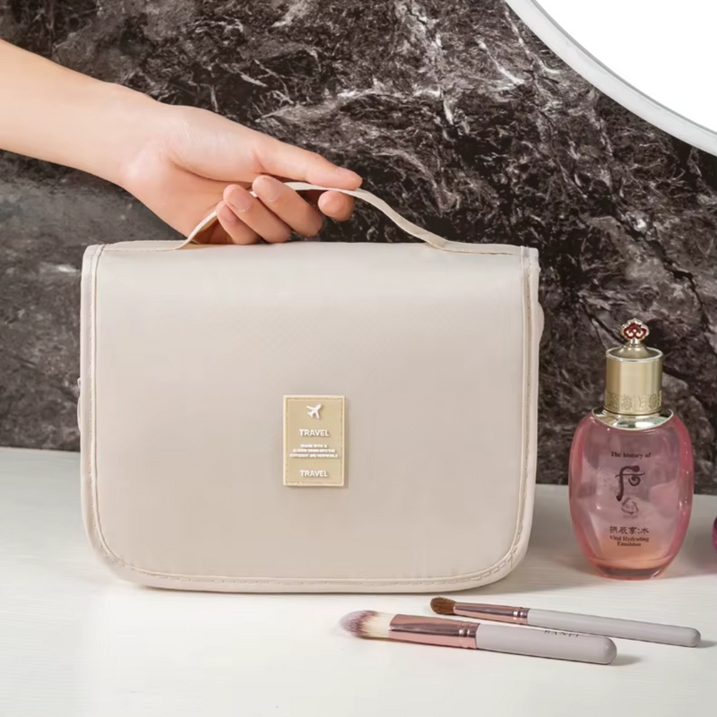 Laden Sie das Bild in Galerie -Viewer, Beige Kulturbeutel mit Griff, ideal für Reisen. Neben Kosmetiktasche stehen Make-up-Pinsel und Parfümflasche auf weißem Tisch. Perfekt für Damen.
