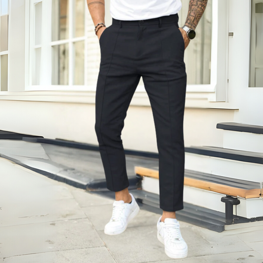 Mann in schwarzer Anzughose und weißen Sneakers vor modernem Gebäude. Stilvolle Herrenmode, urbane Eleganz, lässiger Business-Look.