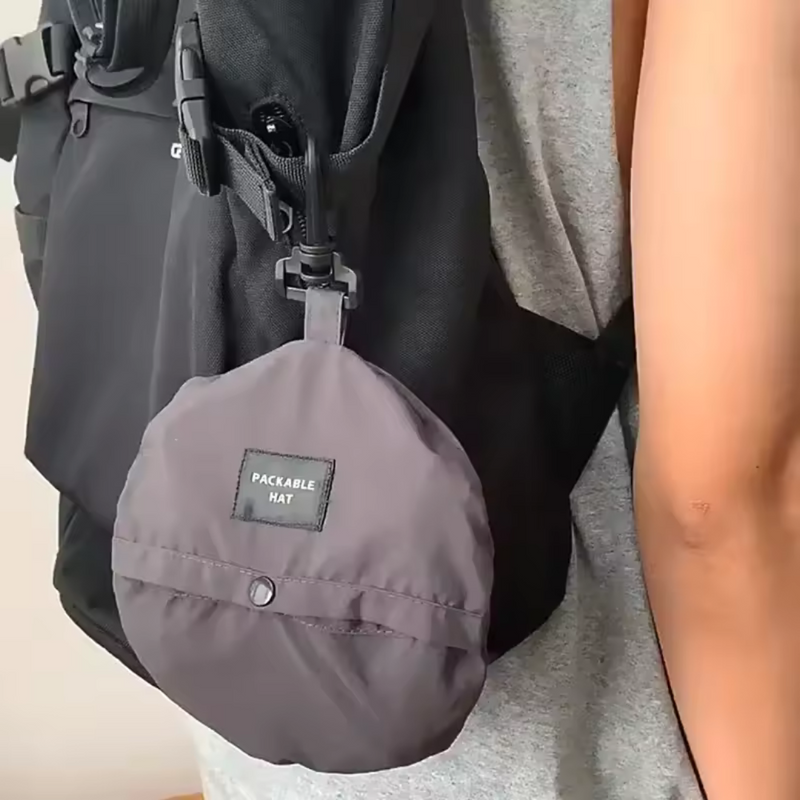 Laden Sie das Bild in Galerie -Viewer, Schwarzer Rucksack mit grauem, faltbarem Hut an der Seite befestigt, getragen von einer Person in grauem T-Shirt. Praktisches Reise-Accessoire.
