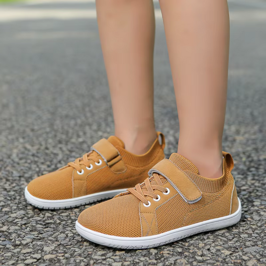 Beige Kinderschuhe mit Klettverschluss und Schnürsenkeln auf Asphalt. Bequeme, atmungsaktive Sneakers für Kinder. Ideal für Freizeit und Sport.
