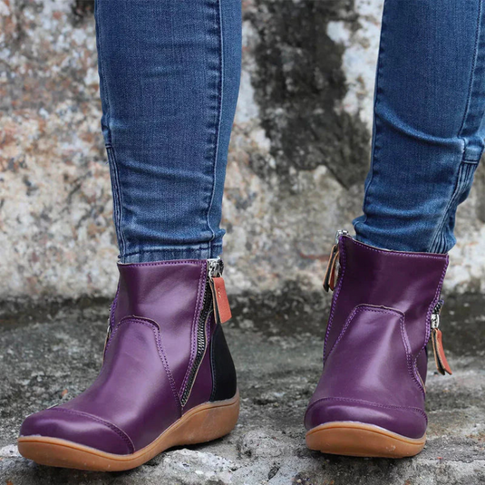 Lila Damenstiefeletten mit Reißverschluss, kombiniert mit blauen Jeans. Modische, bequeme Schuhe für Herbst und Winter auf grauem Hintergrund.
