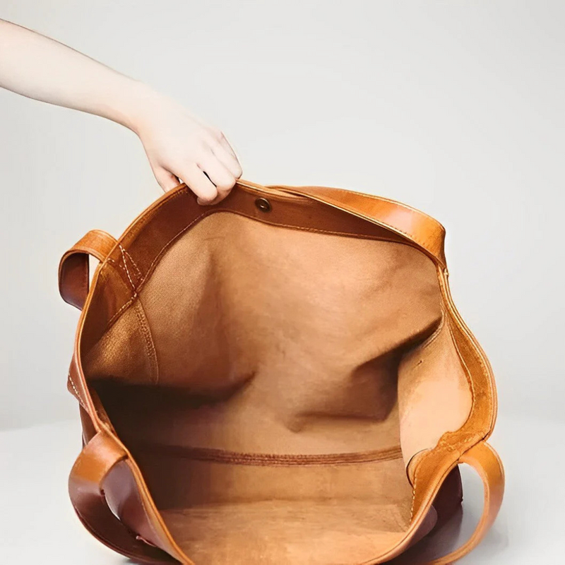 Laden Sie das Bild in Galerie -Viewer, Hand hält offene braune Ledertasche mit geräumigem Innenraum, ideal für Reisen oder Alltag. Hochwertiges Leder, stilvolles Design, langlebig.
