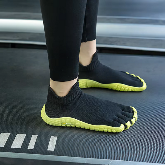Schwarze Zehenschuhe mit gelber Sohle auf Laufband, minimalistisches Design, ideal für Barfußlauf, Fitness, Sport, ergonomische Passform.
